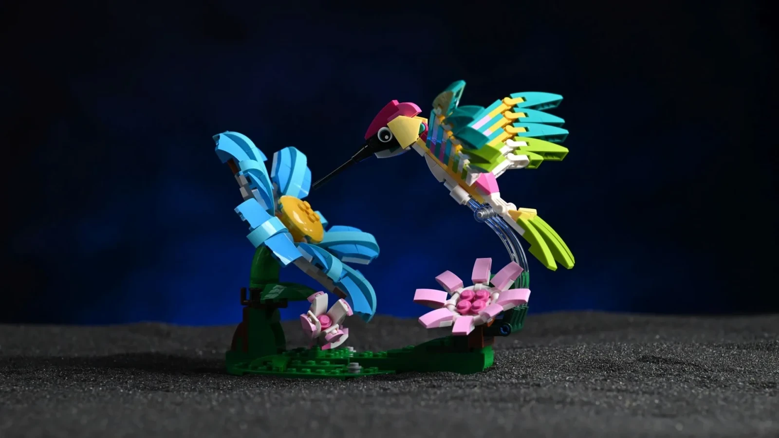 Der LEGO Bunte Kolibri (31384) in dynamischer Flugpose über seinem brick-gebauten Blütenstand