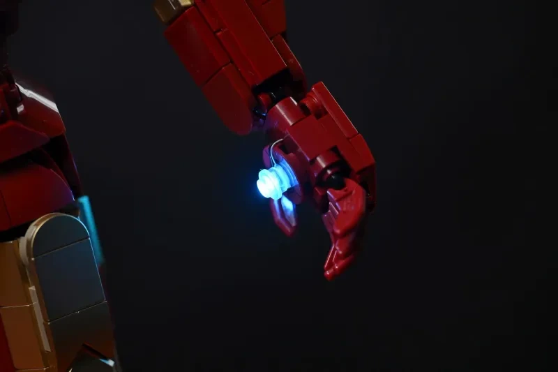 Makroaufnahme der LEGO Iron Man Mark 3 Hand mit blau leuchtendem Handflächen-Repulsor vor schwarzem Hintergrund