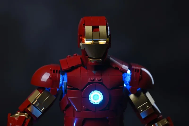 Der Oberkörper der LEGO Iron Man Mark 3 Figur im Dunkeln, Brustreaktor und Schulter-Repulsoren leuchten blau, die Augen golden